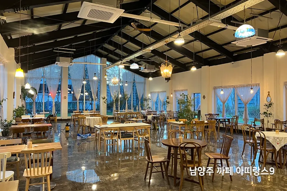 박공지붕 카페 내부, 저녁 조명과 원목 테이블이 어우러진 전경