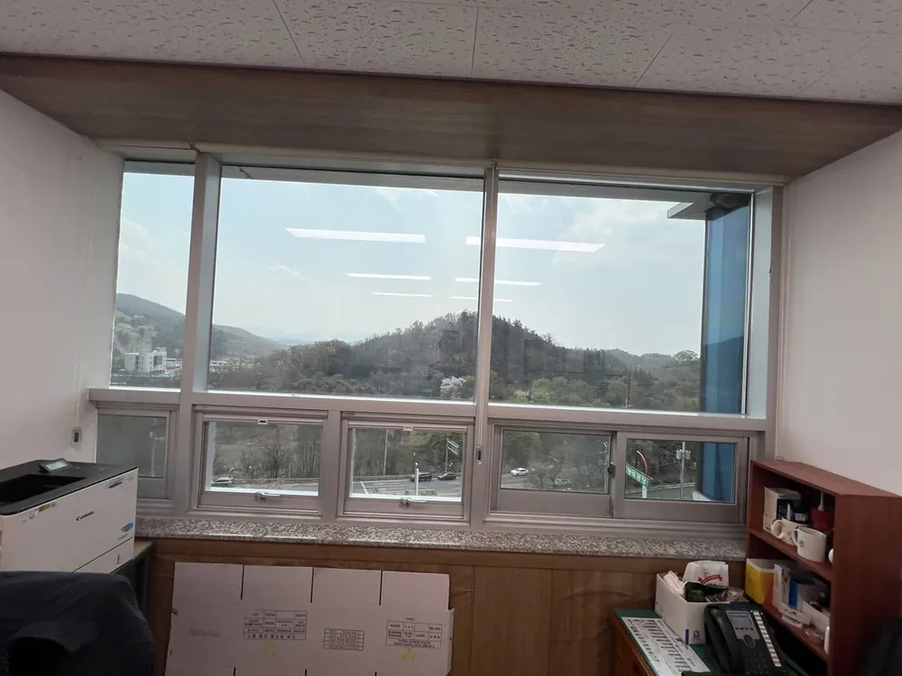 산 능선이 보이는 창가 책상, 화분과 사무기기가 놓여 있다